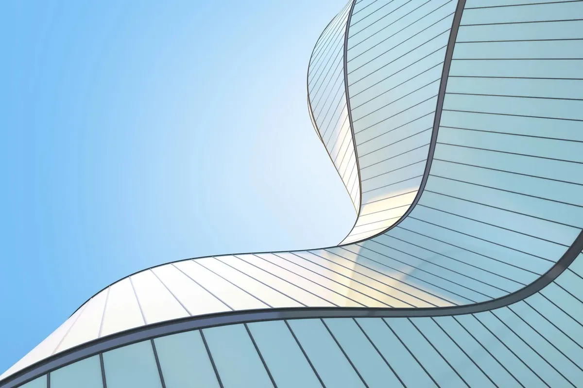 The curved glass facade of an office building seen from below against a clear sky.